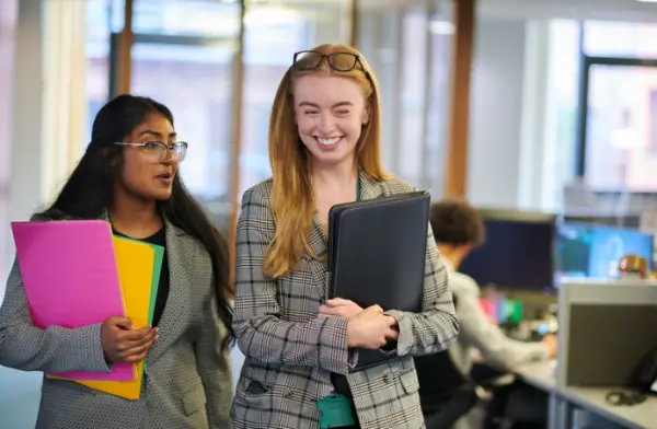 Two people holding files, smiling while having a conversation