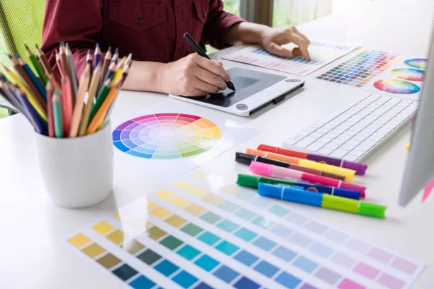 A designer uses a graphics tablet, with color palettes, markers, and colored pencils arranged on a desk, showcasing creative tools.