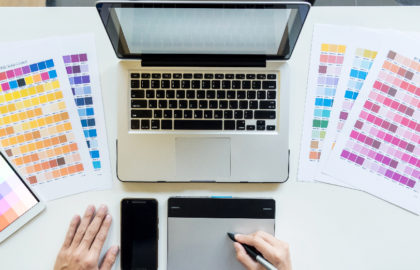 A person designing using a pen and tablet while in front of laptop