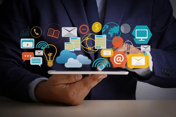 A businessman holds a tablet displaying various digital icons, symbolizing communication, information, and technology connectivity.