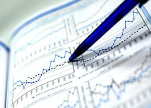 A blue pen points to financial graphs in a report, showcasing various line charts and data trends on a white background.