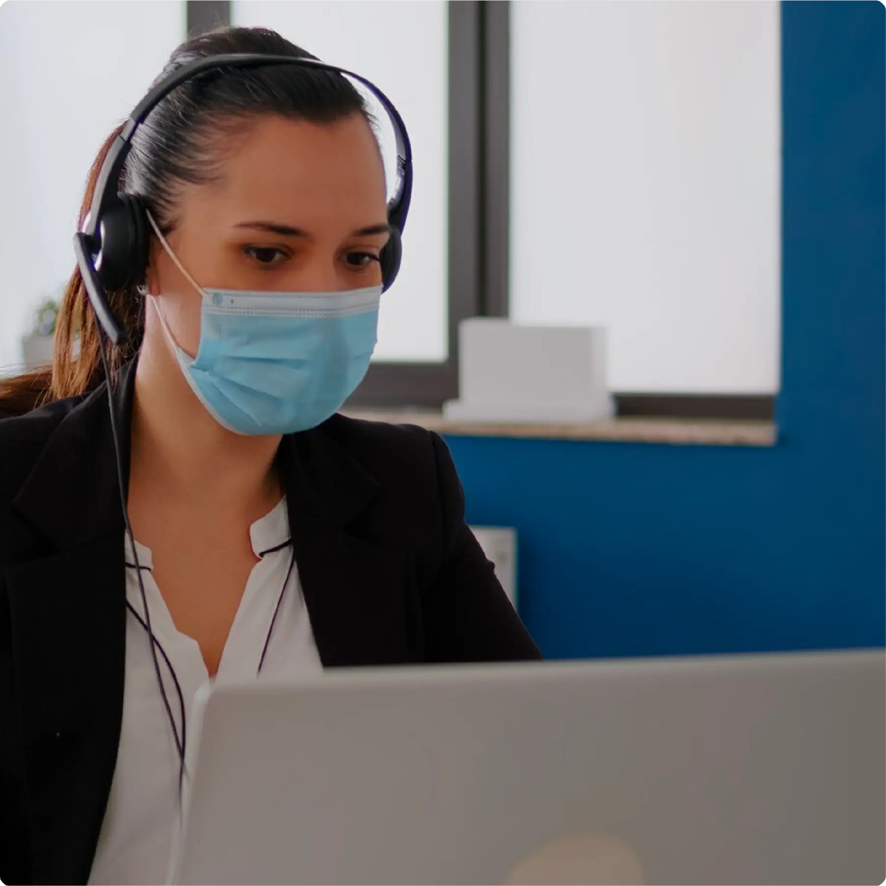 A person with a surgical mask while on headphone in front of laptop